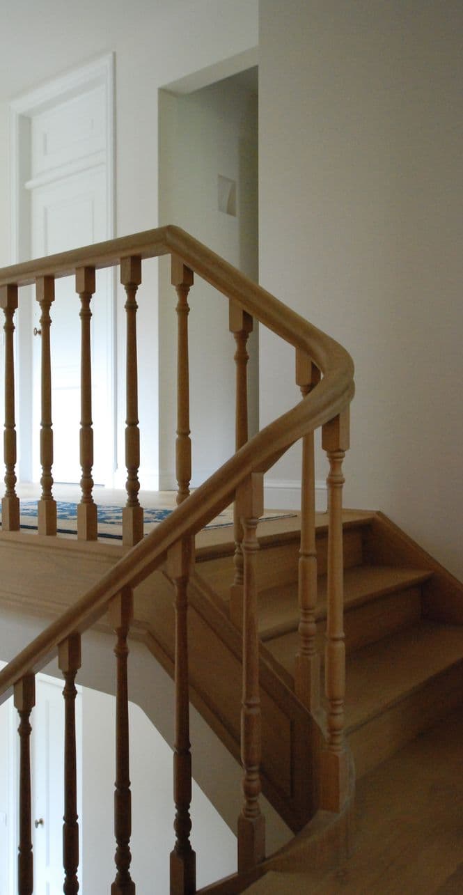 Binnentrap met houten leuning en spijlen, lichte muren en houten treden.