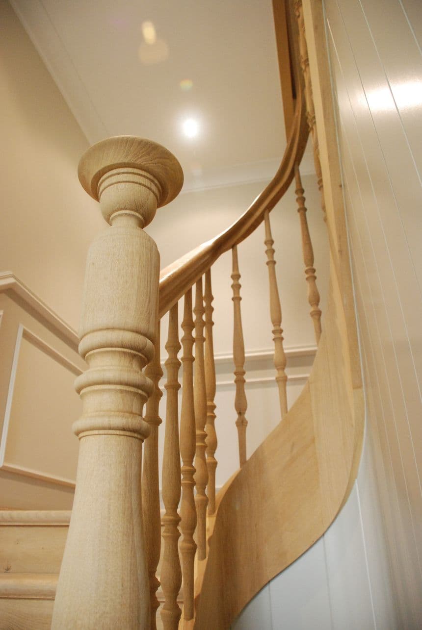 Houten trap met gebogen leuning en gedraaide spijlen, grote ronde newelpaal op de voorgrond.