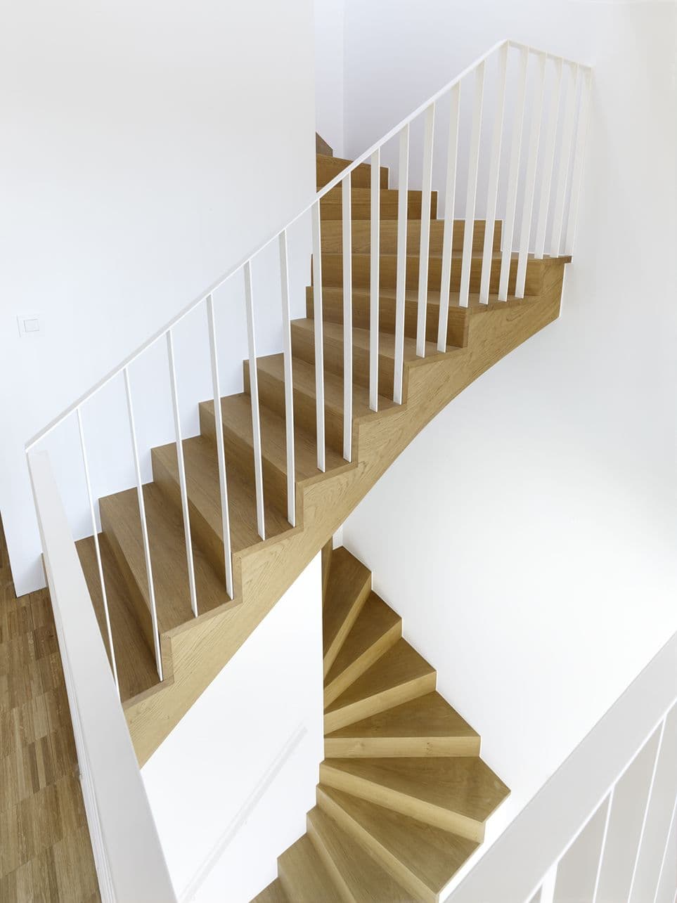 Moderne houten trap met witte balustrade tegen witte muren.